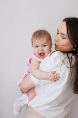 Sweet young mother holding her little 1-year-old daughter in hands.
Caring brunette woman laying with her baby child at home. Tenderness and love between mother and daughter. Lovely family indoors.