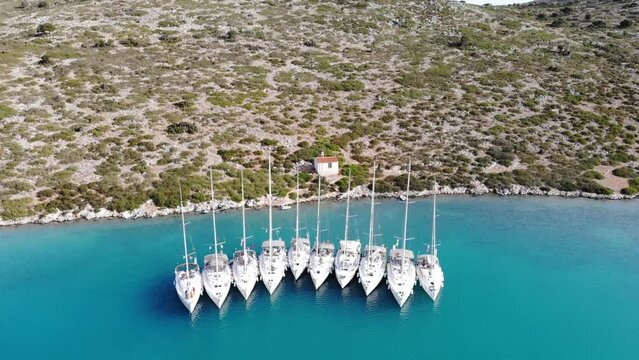 Segelboote als Flotille beim Ankern im P&auml;ckchen nahe Ufer in Griechenland in blauem Meer im Urlaub bei Sonne per Drohne als Luftaufnahme gefilmt
