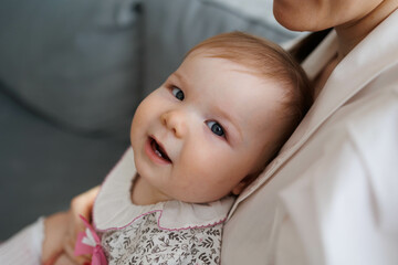 Sweet young mother holding her little 1-year-old daughter in hands.
Caring brunette woman laying with her baby child at home. Tenderness and love between mother and daughter. Lovely family indoors.