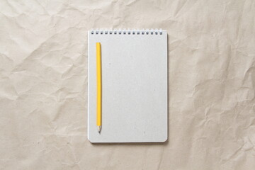 Gray notepad with white coiled spring and pencil on a background of beige crumpled craft paper. With empty space for text and design