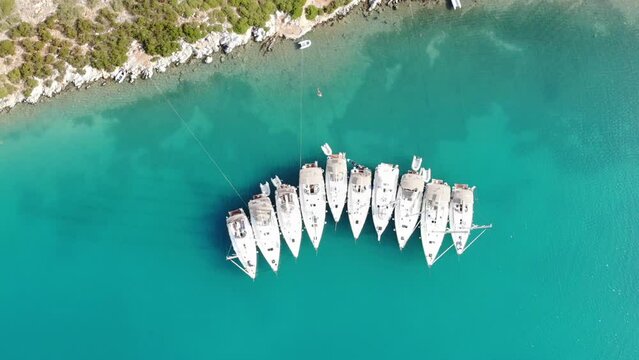 Segelboote als Flotille beim Ankern im P&auml;ckchen nahe Ufer in Griechenland in blauem Meer im Urlaub bei Sonne per Drohne als Luftaufnahme gefilmt