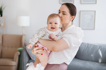 Sweet young mother holding her little 1-year-old daughter in hands.
Caring brunette woman laying with her baby child at home. Tenderness and love between mother and daughter. Lovely family indoors.