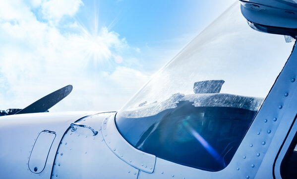Scenery of airplane windshield reflecting harsh sun rays with clouds and bright blue sky, selective focus. Aircraft flying in the sunny day. Small plane. Aviation business concept.