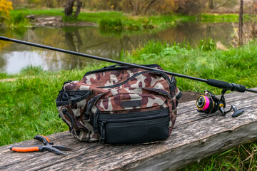 Fishing tackle set. Special angling bag, spinning rod with reel and pliers on wooden log near wild...
