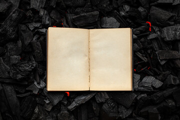 An open book with a black cover on smoldering charcoal. Textured dark back.