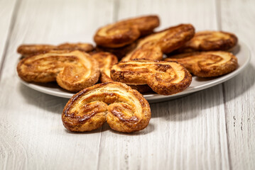 Palmier puff pastry biscuits in white plate on a white painted wooden table