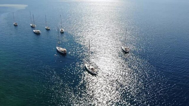 Segelboote als Flotille beim Ankern in Griechenland in blauem Meer im Urlaub bei Sonne per Drohne als Schwenk gefilmt