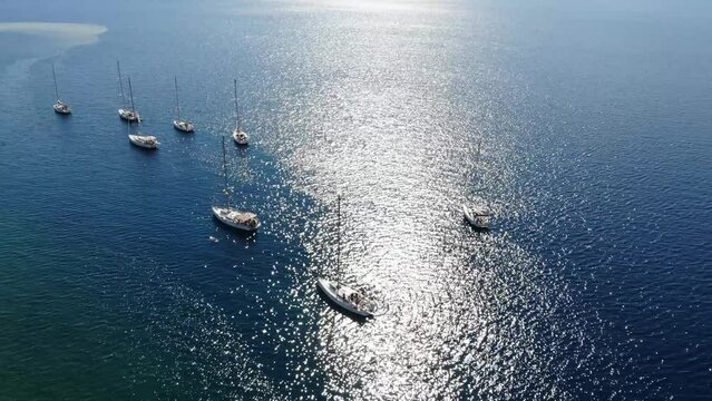 Segelboote als Flotille beim Ankern in Griechenland in blauem Meer im Urlaub bei Sonne per Drohne als Schwenk gefilmt