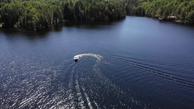 Luftaufnahme von Motorboot fahrend auf Wasser mit Wellen zwischen Inseln mit B&auml;umen in Schweden auf See bei Sonne per Drohne gefilmt
