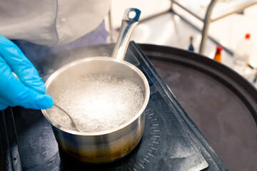 boiling water in a ladle on the stove, a gloved hand stirs the water with a spoon