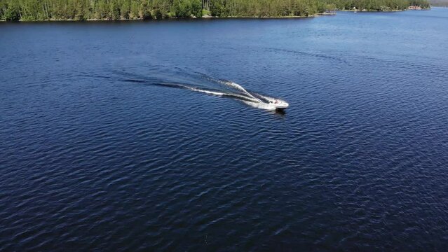 Luftaufnahme von Motorboot fahrend auf Wasser mit Wellen zwischen Inseln mit B&auml;umen in Schweden auf See bei Sonne per Drohne gefilmt