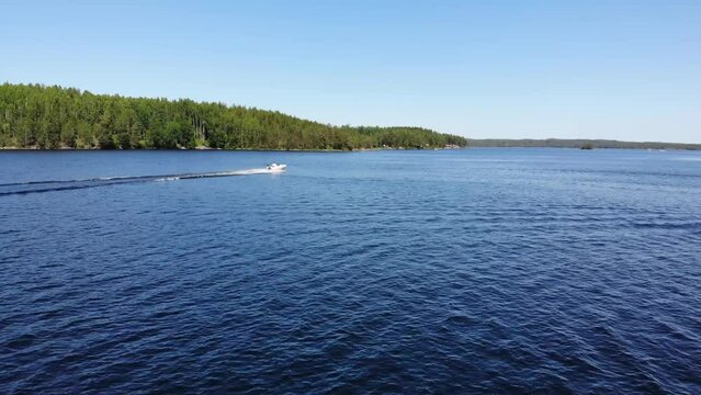 Luftaufnahme von Motorboot fahrend auf Wasser mit Wellen zwischen Inseln mit B&auml;umen in Schweden auf See bei Sonne per Drohne gefilmt