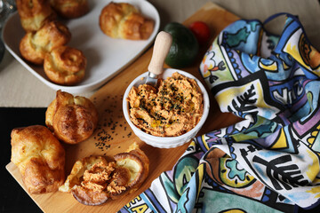 ricotta dip with sun-dried tomatoes and baked paprika in a ceramic white bowl and homemade popover, which is a puffed, airy, and eggy hollow roll, is fresh from the oven