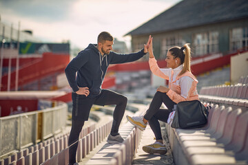 A young couple is giving five to each other while talking at the stadium and waiting for a...