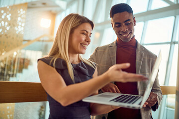 A young business woman is showing a laptop content to a male colleague while standing in the hallway. Business, people, company