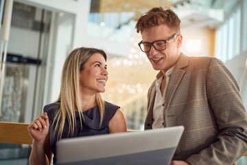 A young business woman is glad showing a laptop content to her young male colleague while standing in the hallway together. Business, people, company