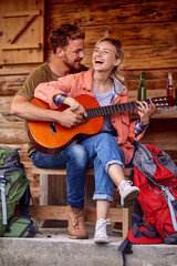 Fototapeta na wymiar A young couple enjoys playing a guitar at cottage porch together. Vacation, relationship, cottage