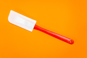 Red and white kitchen spatula made of silicone and plastic insulated on a orange surface