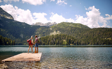 A young couple is standing on the dock at the lake and enjoying the view during mountain hiking. Trip, nature, hiking