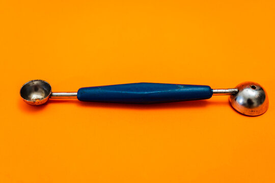 Cooking spoon to make little balls with vegetables or fruits with orange background. Kitchen and pastry utensil.