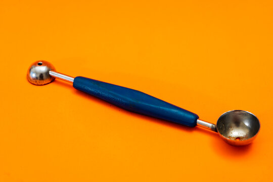 Cooking spoon to make little balls with vegetables or fruits with orange background. Kitchen and pastry utensil.