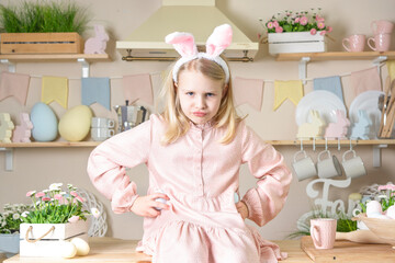 Easter An angry and impatient little girl with rabbit ears sits on a table against the backdrop of...