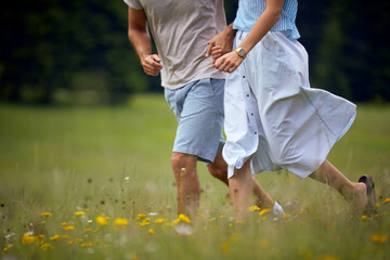 Couple holding hands and running in green meadow. Joyful couple in nature. Fun, togetherness, lifestyle, nature concept.
