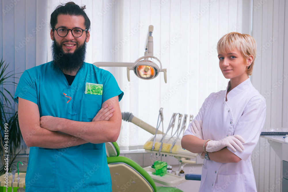 Wall mural Smiling bearded dentist standing with his beautiful young female colleague in their dental office