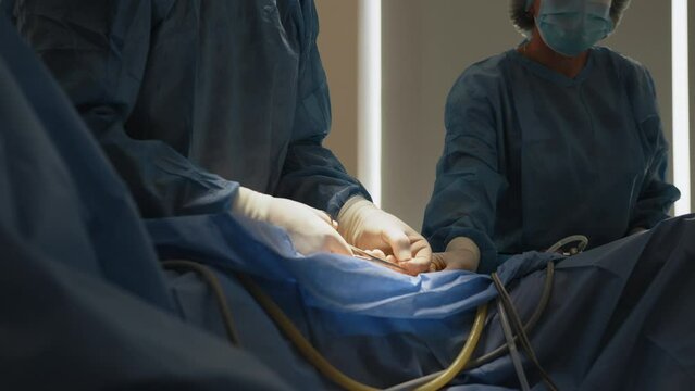 Surgeon ties knots for stitches on open wound. In the Hospital Operating Room Diverse Team of Professional Surgeons and Nurses Suture Wound after Successful Surgery. Professionals Saving Lives