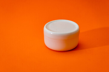 Small white plastic cream jar with lid isolated on orange background.
