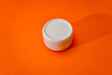 Small white plastic cream jar with lid isolated on orange background.