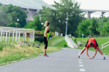 Fototapeta premium Young couple warming up and stretching together in a park before running