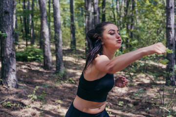 Close up portrait of a sexy brunette exercising kickbox with direct punches in the middle of the forest