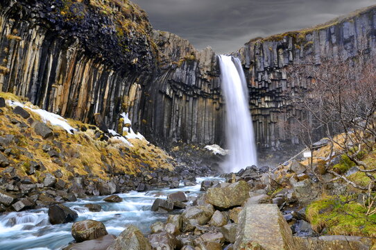 Long exposure picture of Svartifoss waterfall in Skaftafell national park in Iceland. Famous icelandic waterfall with dark dramatic stormy clouds. Black rock and white water. Iceland country side.