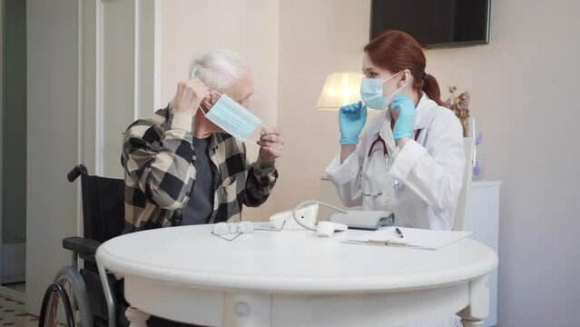  A Doctor Helps An Elderly Disabled Person To Put On A Medical Mask