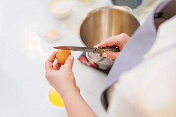 top view. A woman breaks an egg with a knife to prepare cream or dough