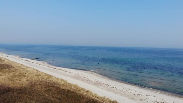 Luftaufnahme von Angler mit Angel in Wathose im Wasser bei Sonne watend per Drohne gefilmt als Fahrt &uuml;ber Strand