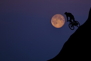 Silhouette of a mountain biker enjoying downhill during full moon evening. Cyclist silhouette on...