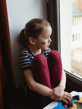 the face of a little girl, a crying child, flowing tears painted on her cheek in the yellow-blue colors of the Ukrainian flag, a request for help.