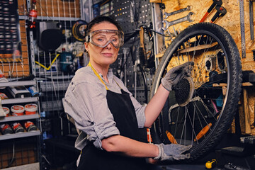 Old female repairman fixing bicycle wheel in repair shop