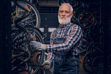 Fototapeta na wymiar Elderly handyman dressed in plaid shirt and overalls around bikes