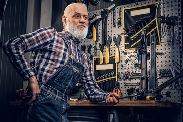 Fototapeta na wymiar Elderly repairman with gray beard leaning workbench in repair shop