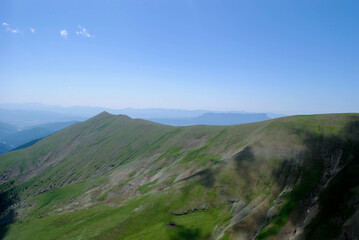 Fototapeta premium Mountainous landscape of long green mountain ranges with a clear blue sky with few clouds