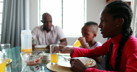 Black family eating meal together, teen daughter drinking orange juice