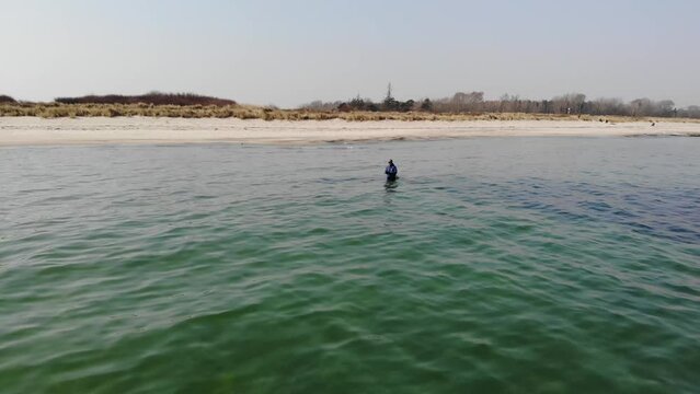 Luftaufnahme von Angler mit Angel in Wathose im Wasser bei Sonne watend per Drohne gefilmt als Schwenk