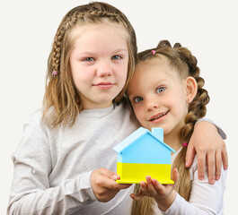 Two little girls calls to Stop war, holding wooden house model in the colors of the flag of Ukraine.  Grey background. Copy Space. No war. Stop war.