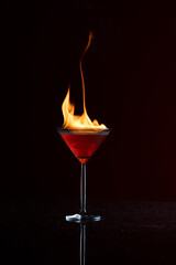 Burning flaming Martini cocktail cosmopolitan with reflection on a black background isolated