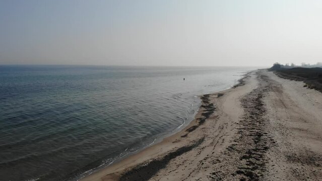 Luftaufnahme von Angler mit Angel in Wathose im Wasser bei Sonne watend per Drohne gefilmt als Fahrt &uuml;ber Strand
