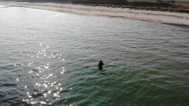 Luftaufnahme von Angler mit Angel in Wathose im Wasser bei Sonne watend per Drohne mit Schwenk gefilmt
