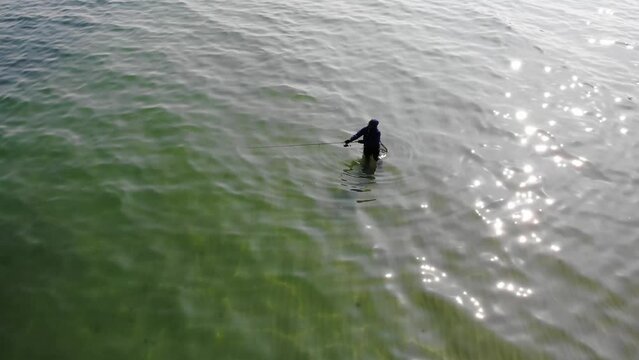 Luftaufnahme von Angler mit Angel in Wathose im Wasser bei Sonne watend per Drohne mit Schwenk gefilmt